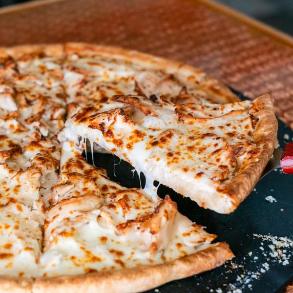 A slice of white pizza with chicken and melted cheese being lifted from a whole pizza.