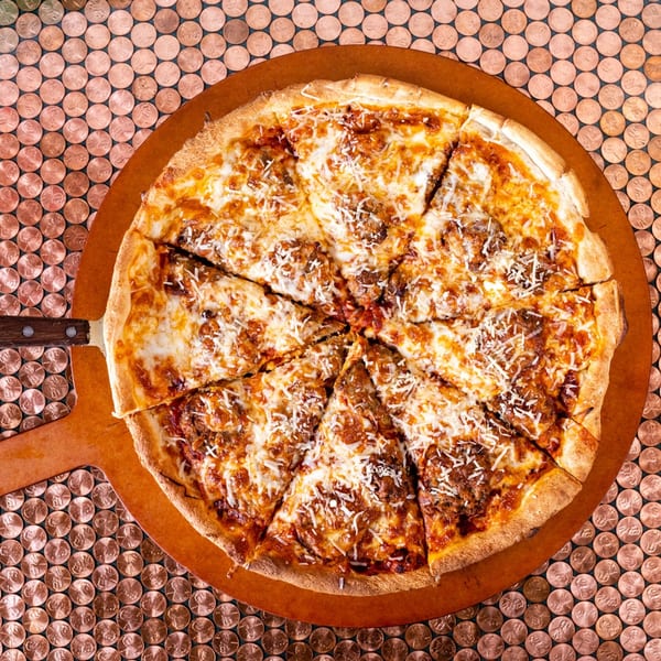 A whole Original Italian Pie pizza, sliced, on a wooden peel over a penny-tiled surface.