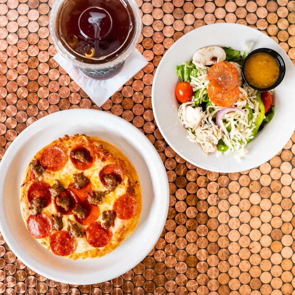 A pepperoni and sausage pizza, salad, and drink on a penny-covered table at The Original Italian Pie.