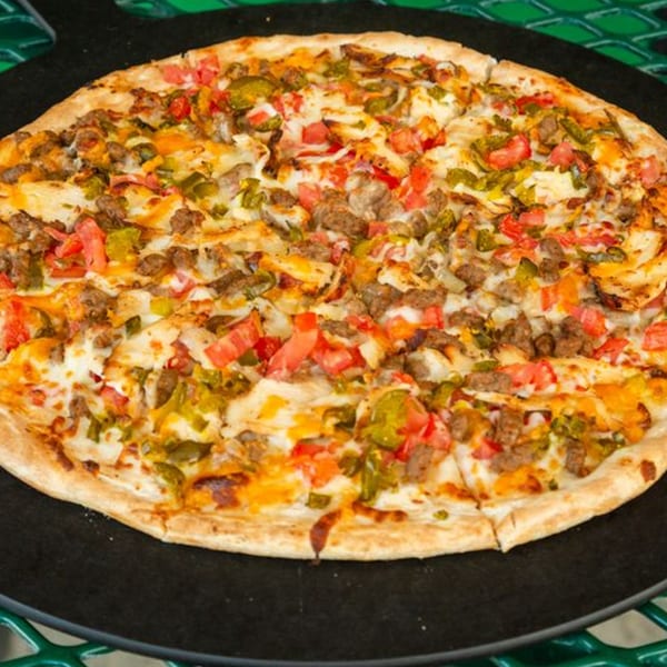 The Original Italian Pie's pizza, topped with sausage, tomatoes, and green peppers, on a black pan.