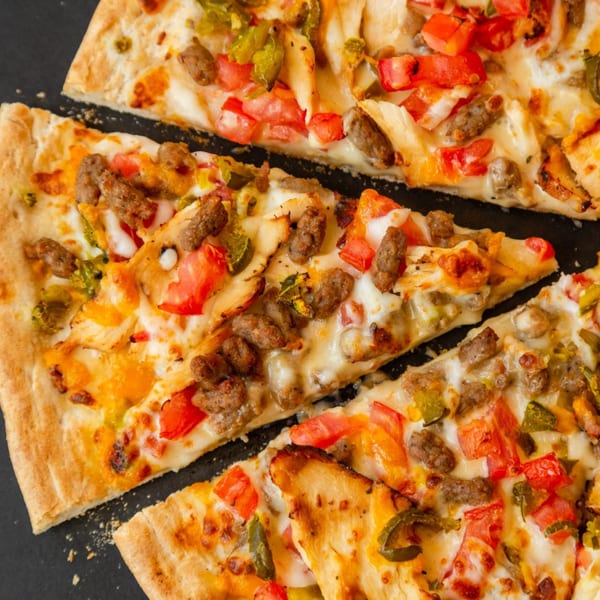 Close-up of sliced Original Italian Pie pizza with sausage, chicken, tomatoes, and peppers.